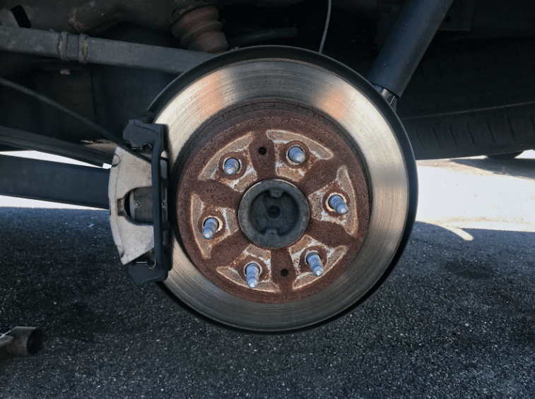 Close-up of a rusty brake rotor and caliper before receiving brake repair service.