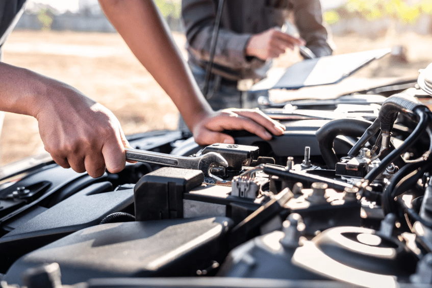 Mechanic performing transmission maintenance on a car engine in an outdoor setting.