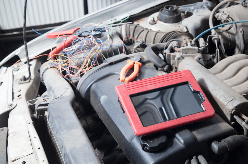 Tablet and tools on a car engine during electronic diagnostics, linking back to the history of auto mechanics.