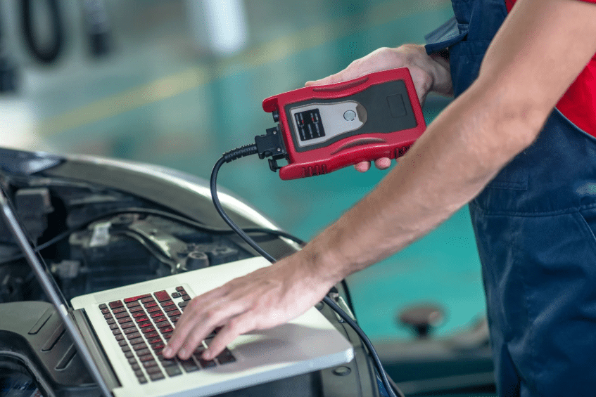 Mechanic connecting diagnostic scanner to a laptop, showcasing current tools shaped by the history of auto mechanics.